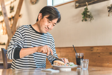 カフェ・飲食店でハンバーガー・ジャンクフードを食べる中高年男性
