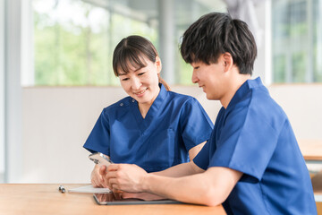 スマホを見ながら会話する先輩看護師と若い男性看護師
