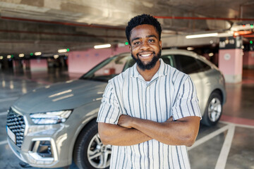 Portrait of casual black man standing at public garage with arms crossed and smiling at the camera.