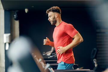 Side view of fit sportsman in shape running on treadmill at gym.