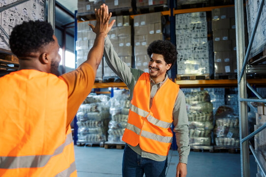 Interracial storage foreman giving high five and encouraging his new employee.