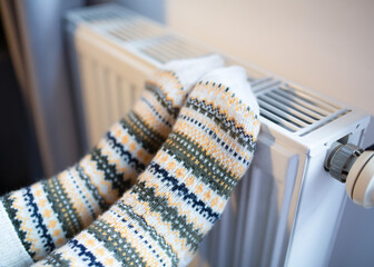 Woman with her feet resting on a radiator to warm them up by the cold of winter and energy saving.