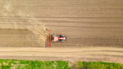 Aerial view of tractor as dragging a seedbed cultivator over agricultural field, farmland