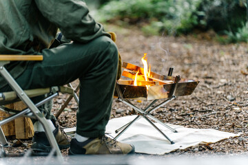 キャンプ場で焚き火する男性キャンパーの後ろ姿
