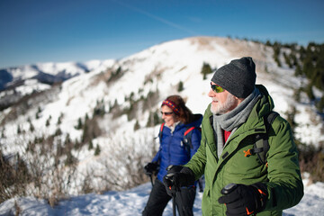 Active seniors enjoying nature. Romantic winter hike for an elderly couple in snowy mountains.