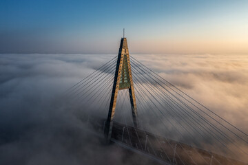 Obraz premium Budapest, Hungary - Aerial view of one of the pillars of the Megyeri Bridge over River Danube covered in heavy autumn fog at sunset with blue and golden sky