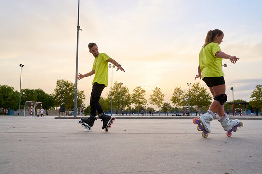 Man and woman practicing synchronized roller skating at sunset in park