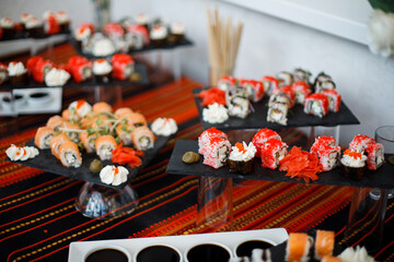 sushi dish placed on a black square plate. The plate features different types of sushi: some are wrapped in nori and topped with white cream and red caviar, others are rolls with white rice.