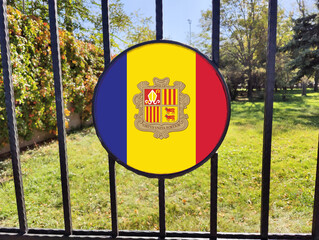 Andorran Flag Framed by Iron Bars: A Tricolor of Heritage, Freedom, and Unity, Encased as a Metaphor for Sovereignty and Perseverance Amidst Boundaries in a Peaceful Green Landscape