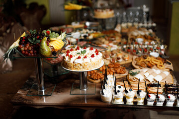 festive table decorated with many desserts. In the foreground are macarons of various colors, including pink and yellow, as well as cakes with colorful layers.