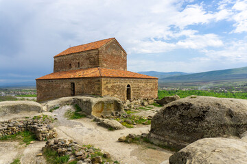 A church with a tiled roof on a hill in an ancient city. Uplistsikhe is an ancient rock-hewn town.