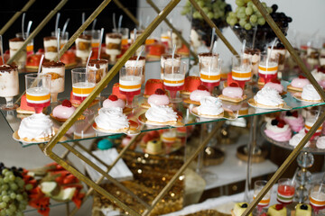 festive table decorated with many desserts. In the foreground are macarons of various colors, including pink and yellow, as well as cakes with colorful layers.