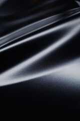 Close-up of a smooth, slightly reflective black fabric showcasing its texture and subtle lighting highlights, creating an elegant and sleek appearance 
