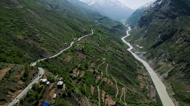 4K aerial view of road passing through mountains along with Chandra river in Lahaul, Himachal Pradesh, India. Drone shot of vehicles driving in mountain road. Road trip, travel and holidays concept.