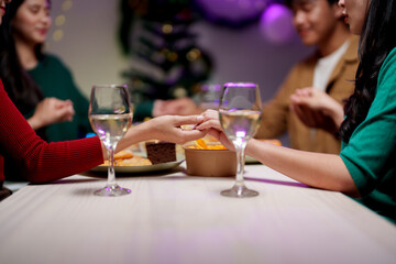 Celebrating Christmas with a group of friends, cheering, Santa hats, gifts, and happy food, wine, and drinks. Hold hands and pray together during the holidays. Holiday celebration ideas.
