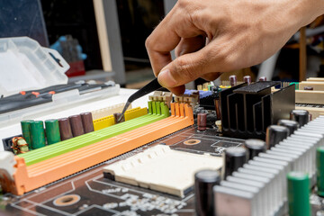 Man technician holding capacitors with tweezers on motherboard circuit board