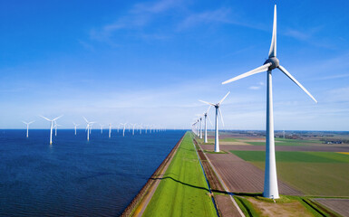 A row of wind turbines stands tall next to a tranquil body of water in the Netherlands Flevoland...