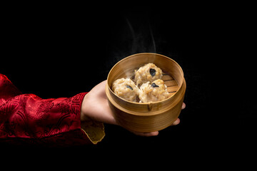 Chinese person holding dim sum dumpling on bamboo wooden basket bowl