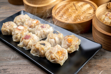 Assorted chinese dim sum dumpling on the plate with bamboo wooden basket bowl on wooden table