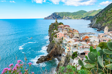 Colorful houses perched along the rocky cliffs of Vernazza Italy while waves lap gently at the...