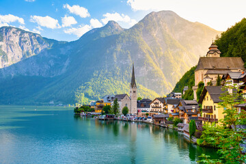 Amidst towering mountains, charming houses imbue Hallstatt Austria with vibrant colors along the lakeside. The golden sunlight dances on calm waters, creating a picturesque reflection at dusk.