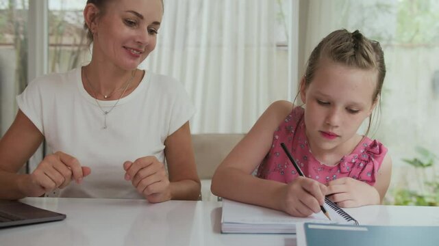 Handheld shot of Caucasian girl listening to mother helping her with difficult homework tasks at home table