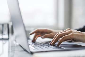 The image captures female hands in close detail, typing on a sleek laptop keyboard, with a fuzzy...