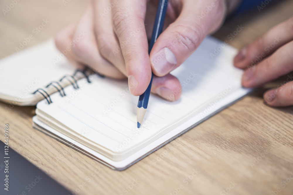 Poster Close perspective of a man's hand making entries in a notepad, with a soft blur in the surrounding