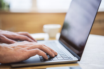 With an office backdrop appearing blurry, a close-up presents a man's hands typing on a...