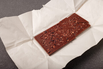 whole but broken bar of dark chocolate with grinded cocoa beans on kraft paper package, close up...