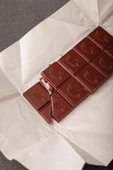 whole but broken bar of dark chocolate with grinded cocoa beans on kraft paper package, top view.