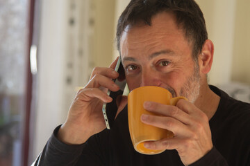 Mature man drinking a cup of coffee and talking on mobile phone