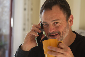 Mature man drinking a cup of coffee and talking on mobile phone