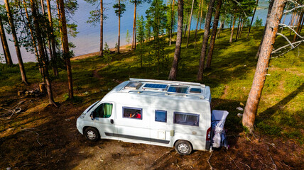 A white camper van with solar panels on the roof is parked in a forest clearing in Finnish Lapland, a lake visible in the distance. © Fokke Baarssen