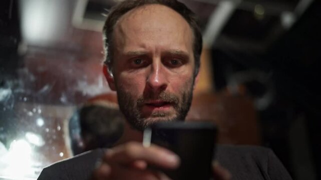 A close-up shot of a man holding an object in a dimly lit room. The scene captures a moment of focus and introspection, with the man's expression conveying a sense of concentration and calm