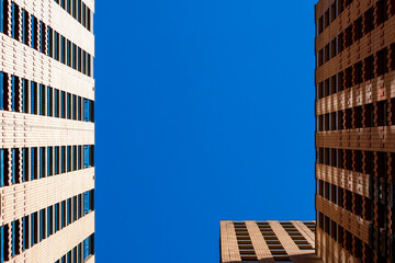 This photograph showcases a captivating upward perspective of urban architecture against a vibrant blue sky, highlighting the symmetry and structure of modern buildings in Amstedam