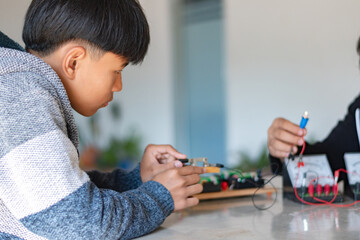 Children are studying electrical circuit systems by experimenting with electrical connections using a small electric meter and a small flashlight bulb in physics science class, soft focus.