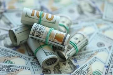 Many rolls of one hundred dollar bills lies on big amount of american currency banknotes