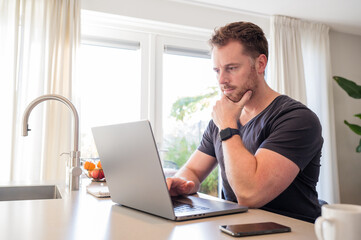 Working at home in the kitchen. caucasian male sitting at the kitchen counter behind his laptop...