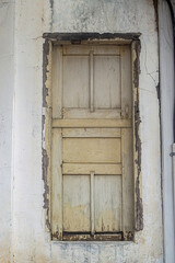 An old, weathered wooden window with peeling paint and cracks in the surrounding wall, showcasing rustic charm and historical character