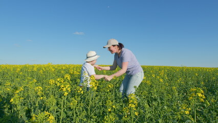 Fototapeta premium Young Mother With Son Enjoy Playing With His Mom In Yellow Rapeseed Field Countryside. Happy Little Boy With Hat. Countryside.