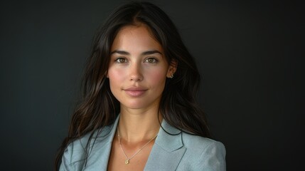 Obraz premium Portrait of a young woman with long brown hair wearing a light blue blazer against a dark background.
