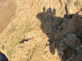 A unique coastal scene featuring the shadows of adventurers projected onto a rugged, sunlit cliff.