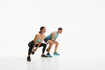 Athletic young man and woman with fit bodies training, doing exercises with kettlebell, showing strength and endurance against white studio background. Concept of sport, active and healthy lifestyle