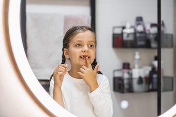 Portrait of young Caucasian girl examining lost tooth in bathroom mirror, showcasing childhood milestone. Expressive emotion captured in modern bathroom setting.