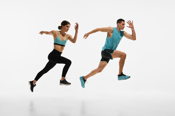 Full-length dynamic image of young athletic couple, man and woman with fit bodies in motion, running against white studio background. Concept of sport, active and healthy lifestyle, workout, fitness