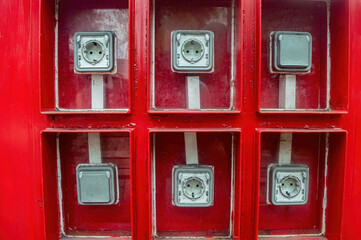 A vibrant red charging station with six electrical outlets enclosed in glass compartments, offering a practical solution for public charging needs.