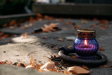 Purple remembrance candle surrounded by autumn leaves on a mossy surface, symbolizing seasonal reflection and honoring traditions.