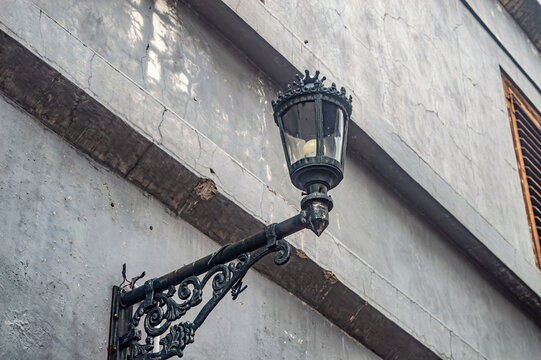 A vintage street lamp mounted on a weathered wall with intricate metalwork, showcasing urban decay and historical charm