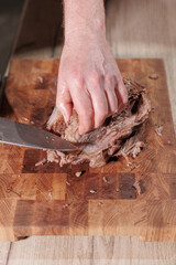 Male hands cutting cooked meat beef on a wooden board